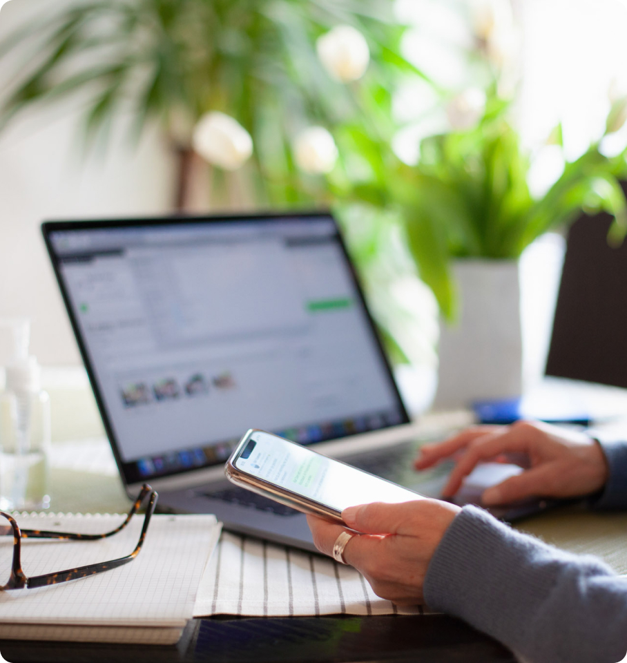 Image of female holding iPhone while simultaneously working on computer.