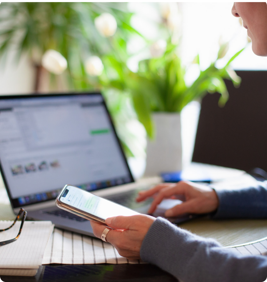 Image of female at a desk working simultaneously on her computer and iphone.